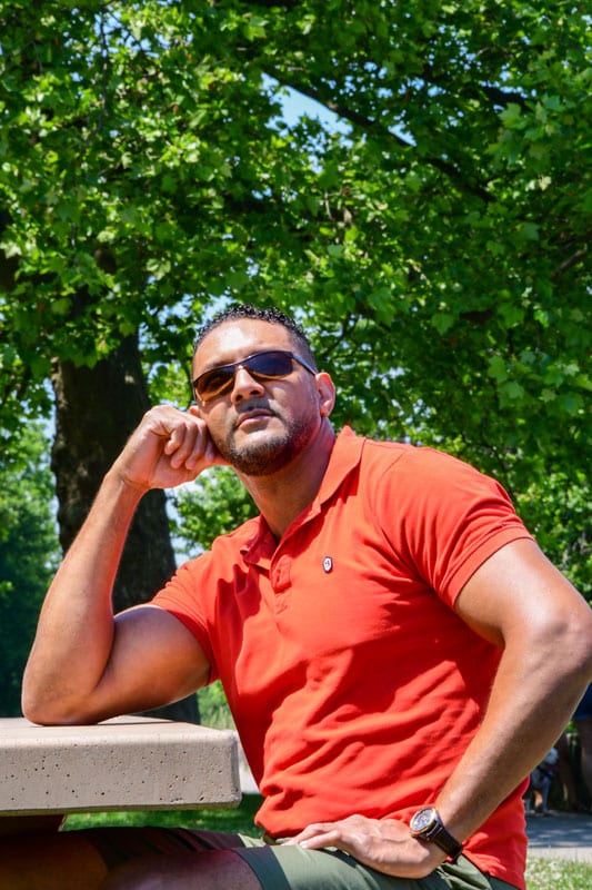 male model in red polo sitting at a table in the park