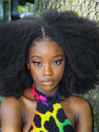 young woman dark skin tones with curly hair wearing a multi-colored dress  