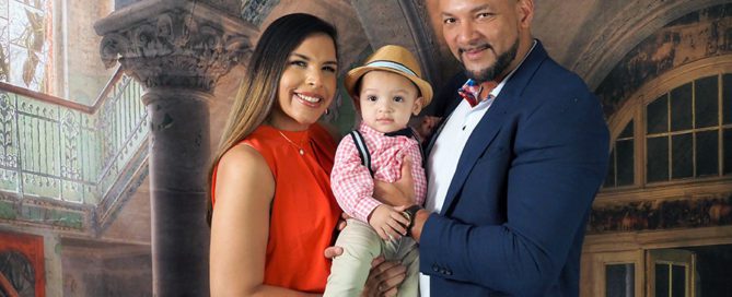 professional studio photo of family portrait. Mother in red dress, boy held by parents in plaid shirt, and man in blue suit